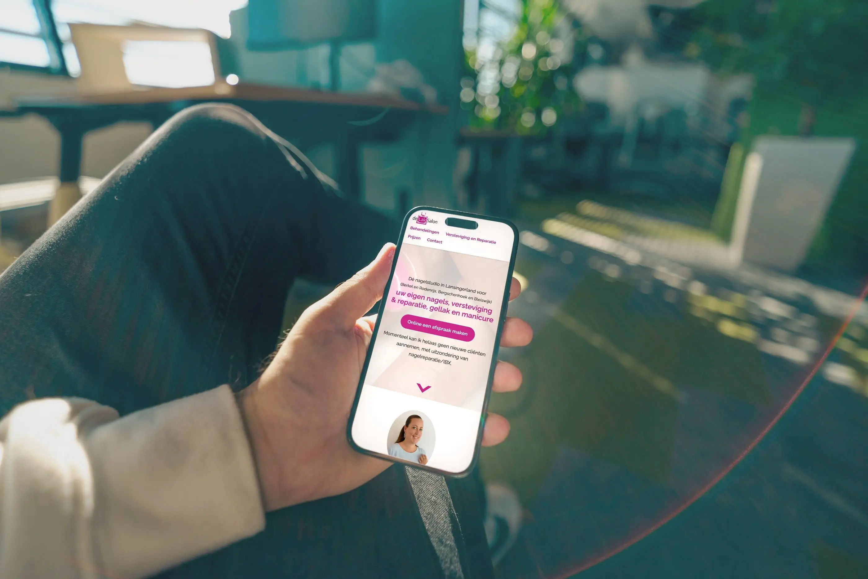 De website van De Lak Salon op het scherm van een telefoon in iemands hand.